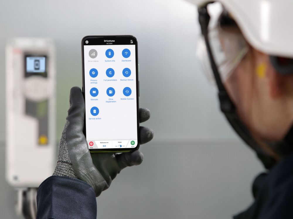 Person in protective gear holding a smartphone displaying an application interface with options like Drive Status, System Info, Dashboard, and Mobile Connect