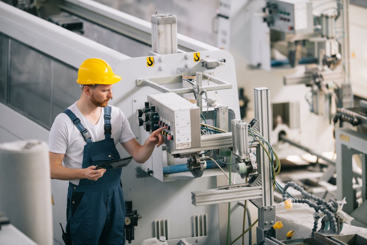 Man with helmet working with machinery in factory.