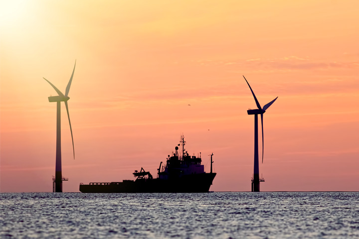 Offshore wind farm vessel next to Offshore wind mills during sunset